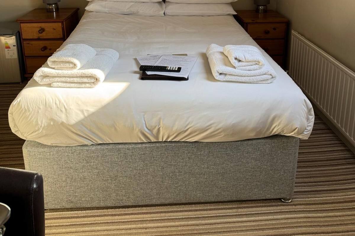 A neatly made bed with pillows, a remote control, and folded towels. There are two bedside tables with lamps.