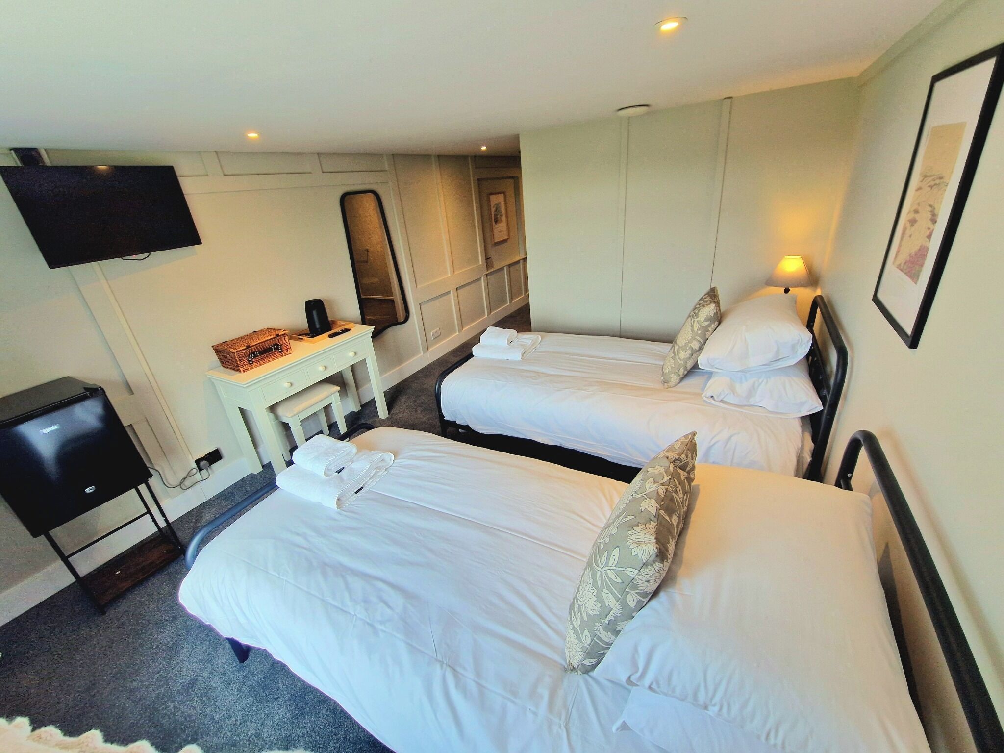A hotel room with two beds, a desk, a television, and a mirror.