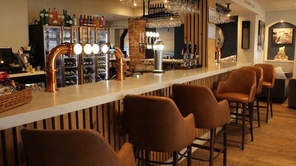 Zona de bar con grifo de cobre, taburetes y un enfriador de vino al fondo.