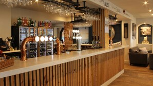 A bar area with a wooden counter, multiple taps, and a variety of bottles. - Dormy House Hotel (Cromer)