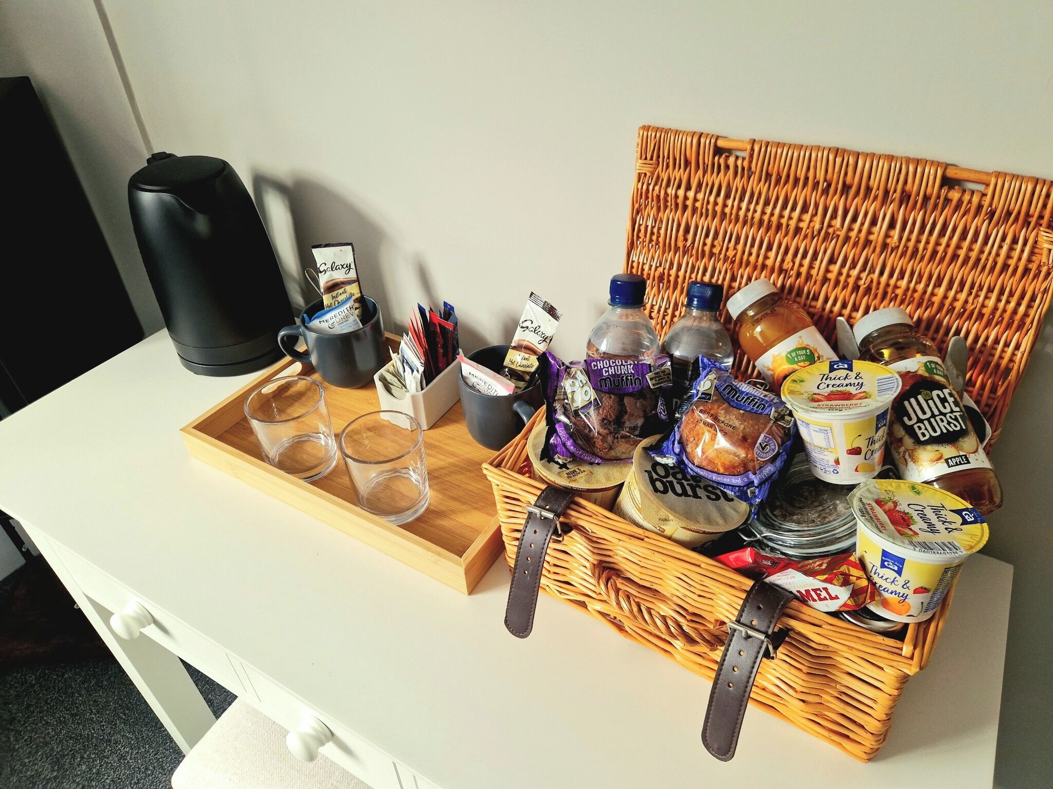 Una bandeja con vasos, una cafetera y una cesta de mimbre con aperitivos y bebidas.