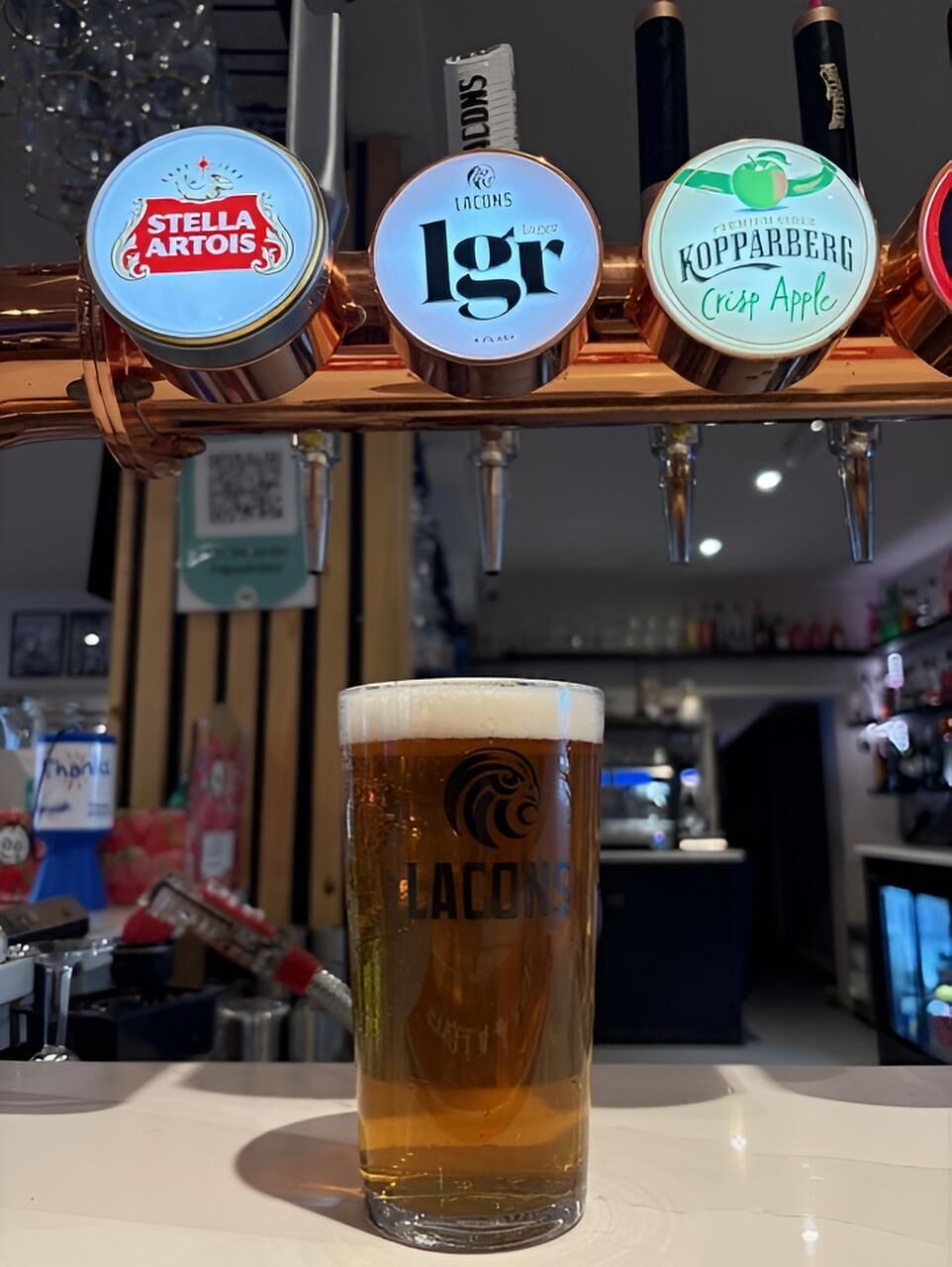 A tap with three beer labels and a glass of beer in front of it.
