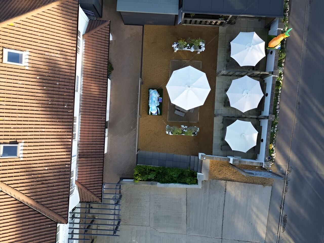 Vista aérea de un patio con mobiliario exterior, sombrillas y una pequeña fuente de agua.