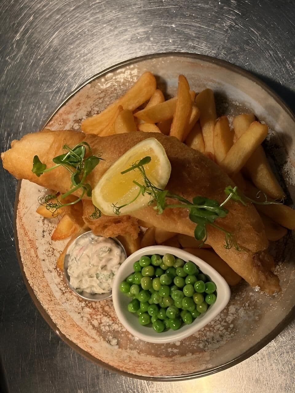 Un piatto di fish and chips con piselli e spicchi di limone.
