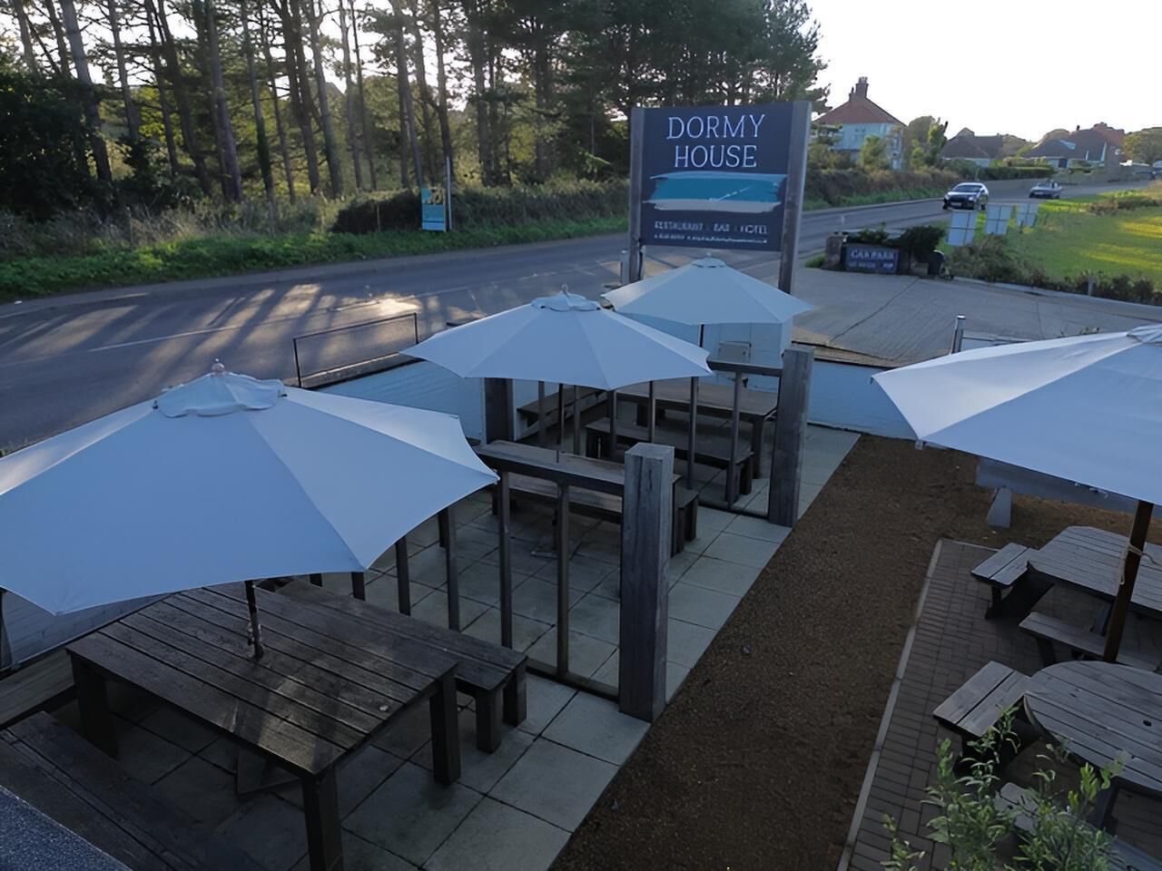 Outdoor seating with umbrellas, a sign for 'DORMY HOUSE,' and a road in the background.