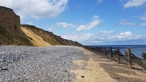 A pebble beach with a wooden jetty, cliffs, and a clear sky. - Dormy House Hotel (Cromer)