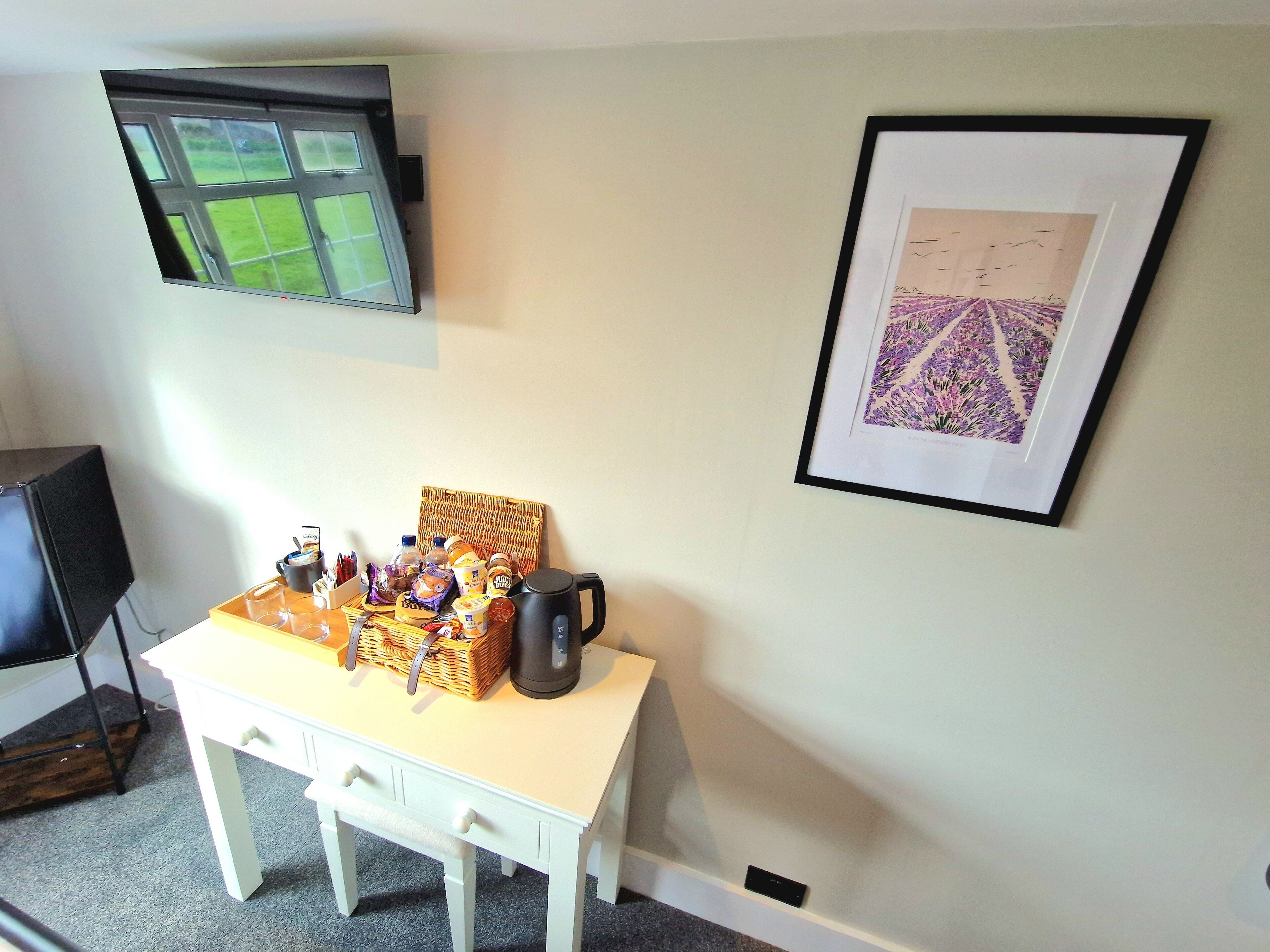 A room with a white table, a black TV mounted on the wall, and a framed picture of purple flowers.
