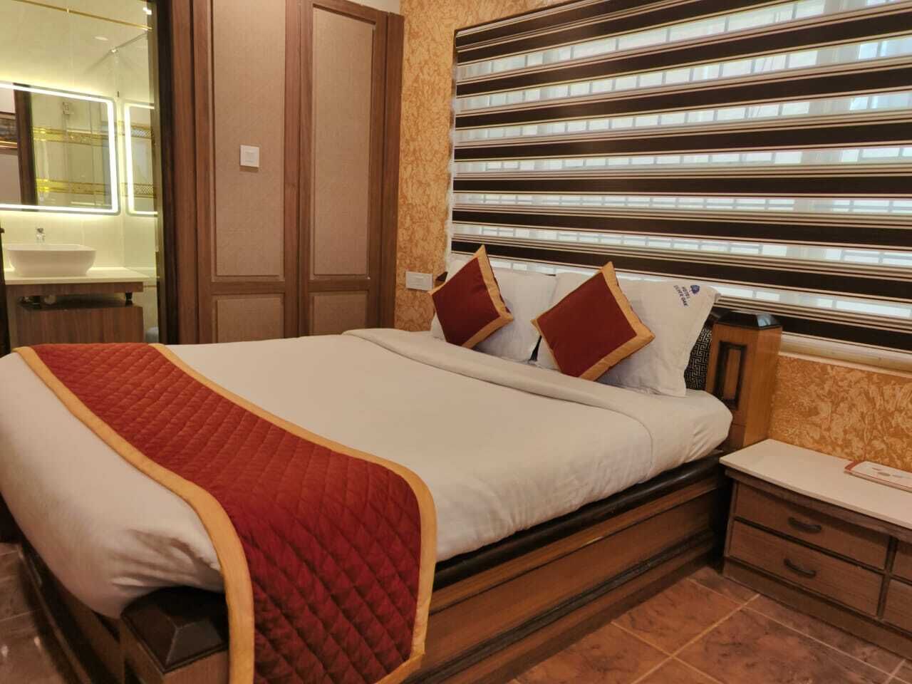 A hotel room with a bed, bedside table, and a large window with blinds.