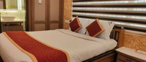 A hotel room with a bed, bedside table, and a large window with blinds.