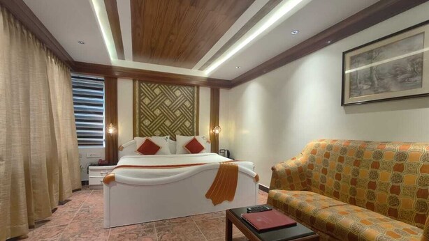 A hotel room with a bed, a sofa, a small table, and a patterned wall. - Hotel Silver Oak (Ootacamund)