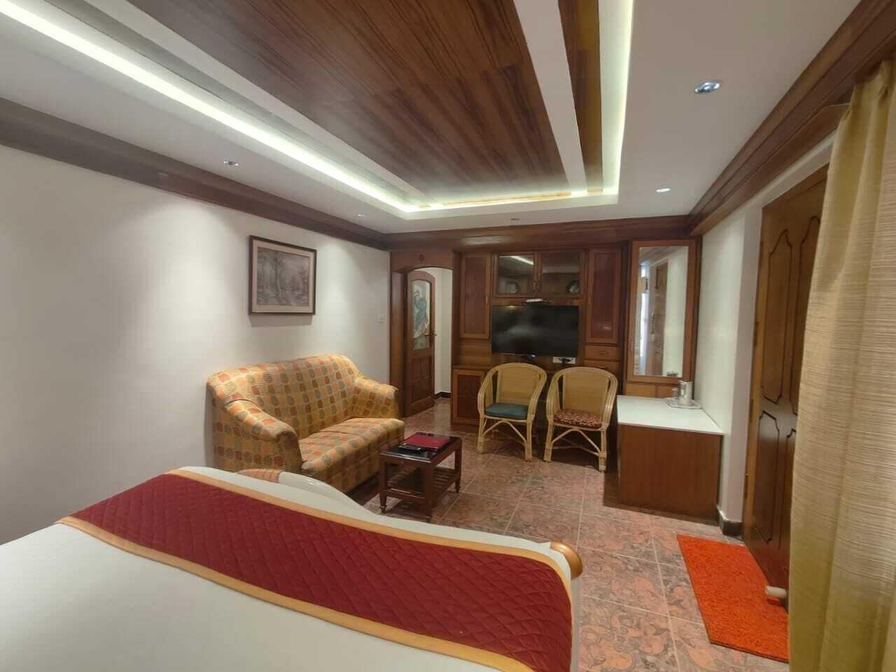 A hotel room with a bed, a sofa, two armchairs, a small table, a TV, and a desk.