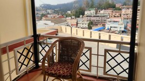 A balcony with a wicker chair, offering a view of a cityscape with buildings and hills. - Hotel Silver Oak (Ootacamund)