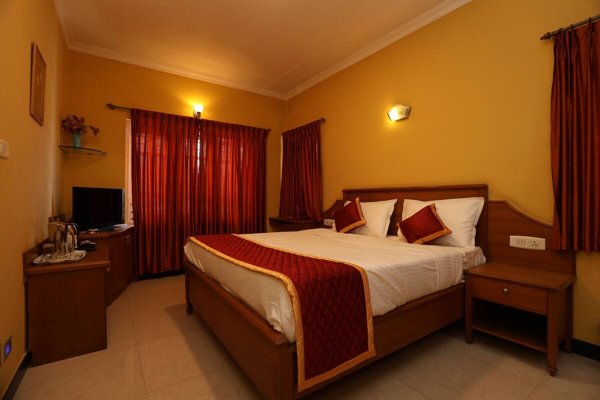 A hotel room with a large bed, wooden nightstands, a desk with a television, and red curtains.