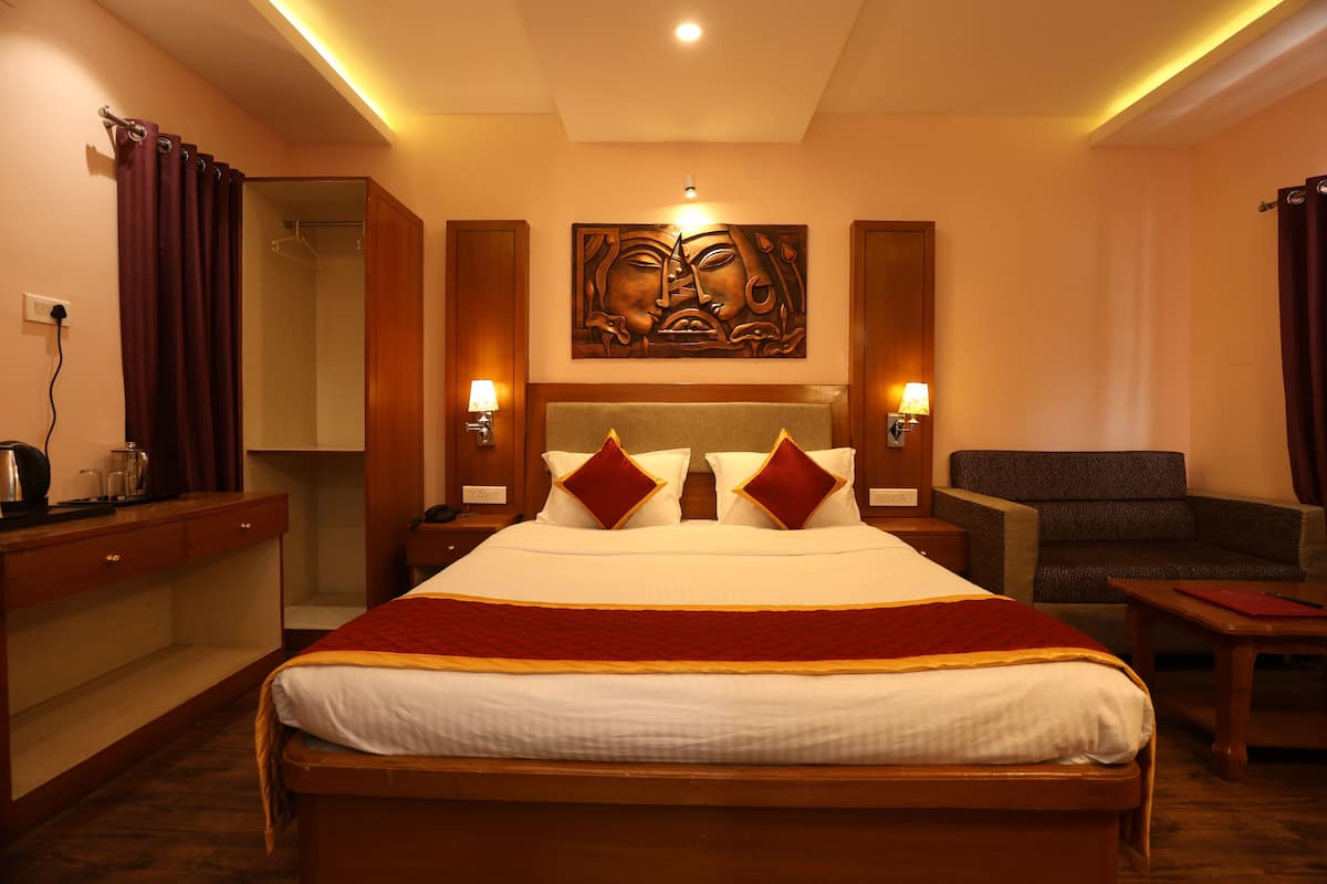 A hotel room with a large bed, two bedside lamps, a wooden headboard, a wall-mounted artwork, a seating area with a chair, and a desk with a lamp.