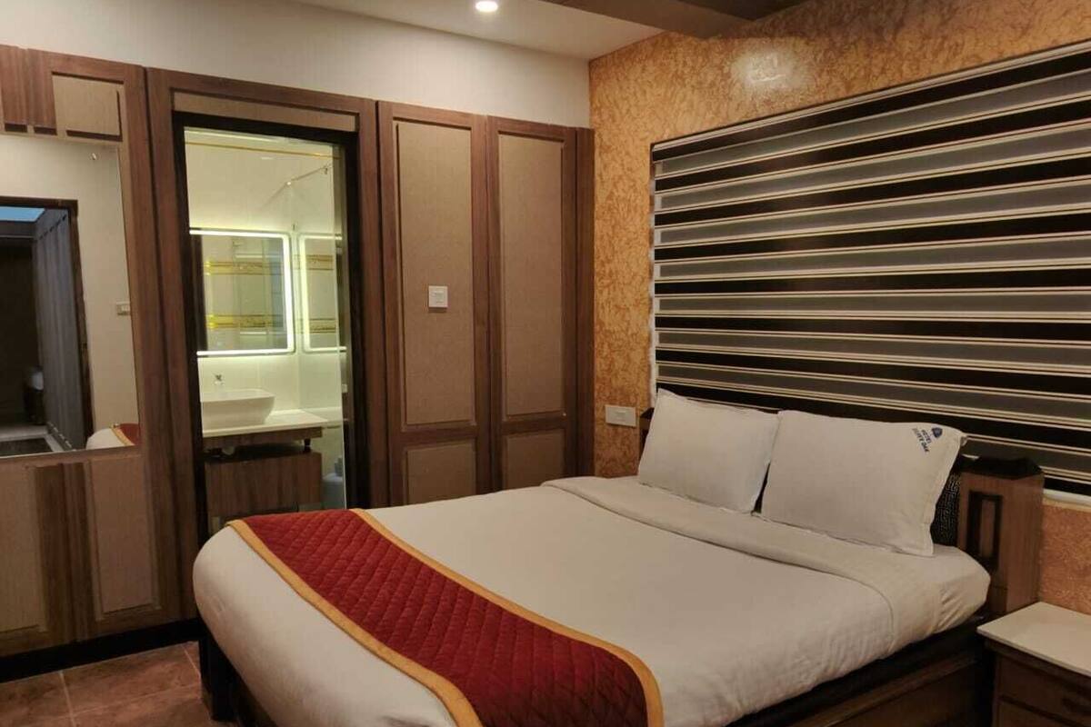 A hotel room with a bed, a wooden wardrobe, a mirror, and a bathroom visible through an open door.