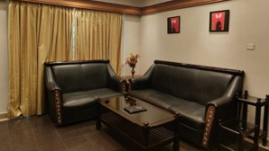 A room with a dark leather sofa, a wooden coffee table, and a vase with flowers. - Hotel Silver Oak (Ootacamund)