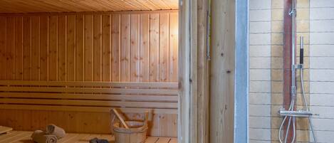 Una sauna con bancos de madera, un balde de madera y zona de ducha con manguera.