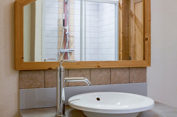 Un baño con un lavamanos blanco, un espejo con marco de madera y una ducha visible en el reflejo.