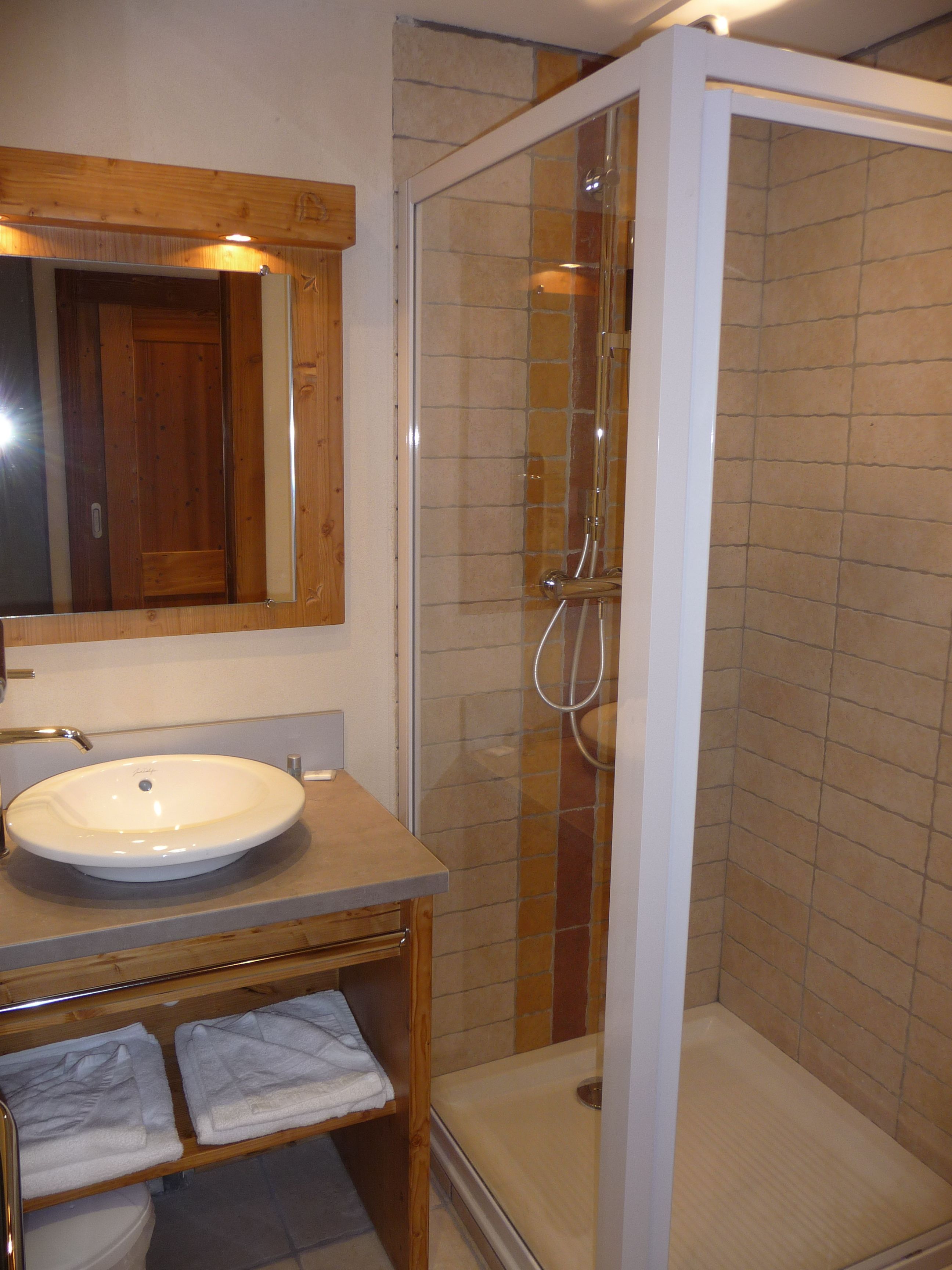 A bathroom with a wooden vanity, a white sink, a glass-enclosed shower, and a mirror above the sink.