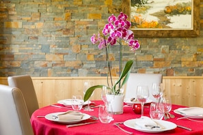 Mesa de jantar posta com pratos, talheres e copos de vinho, com uma orquídea em vaso no centro.