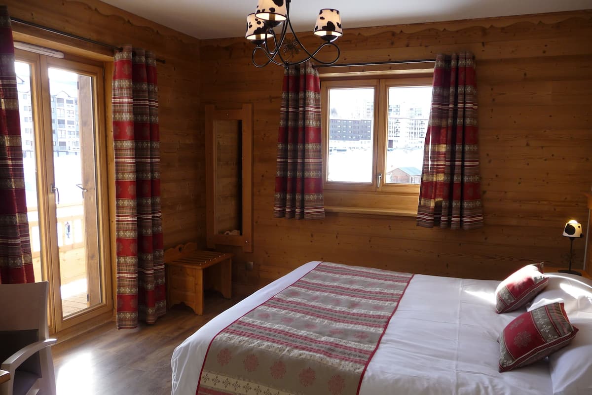 A wooden room with a bed, curtains, and a window.