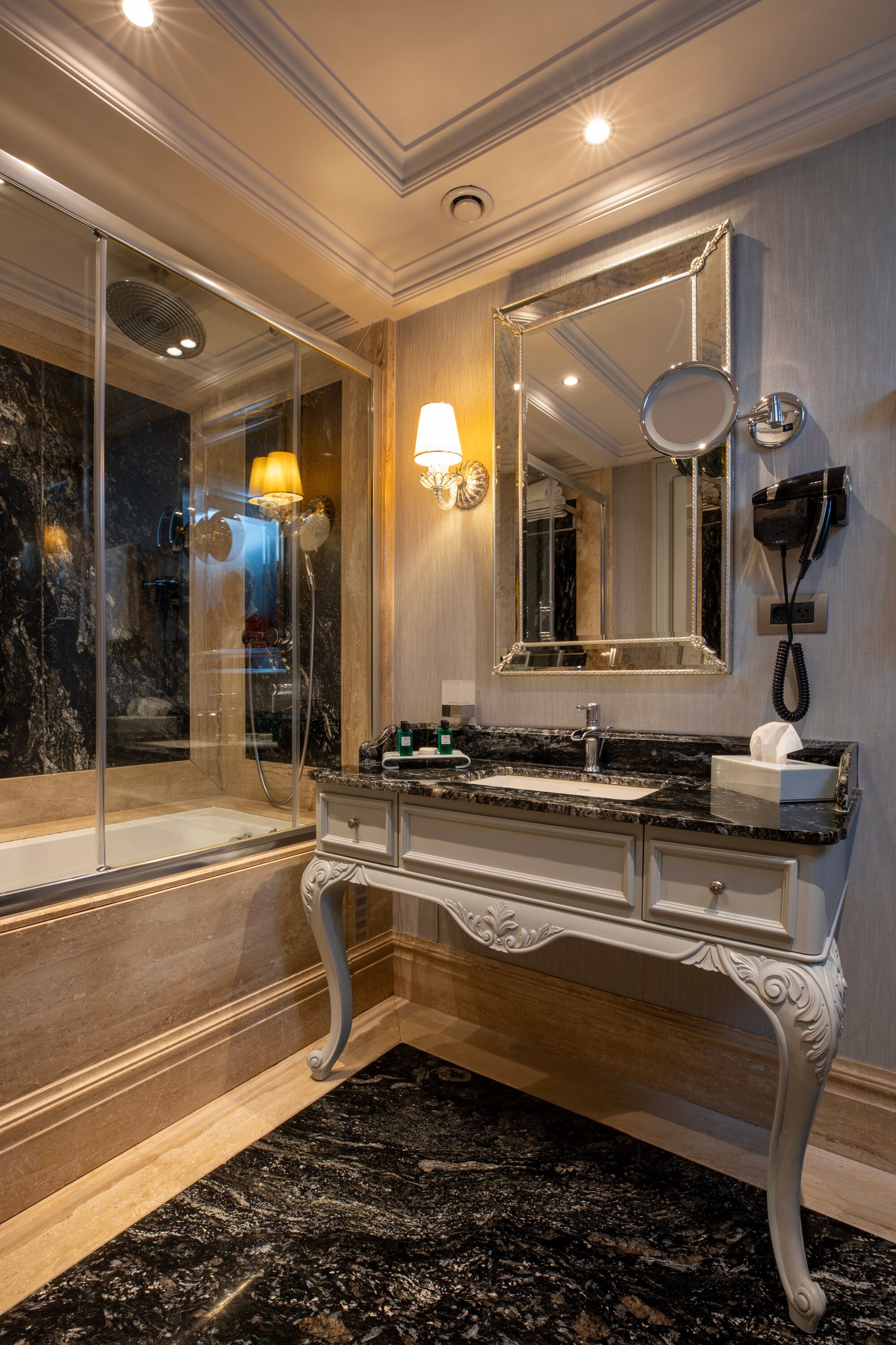 A luxurious bathroom with a marble sink, a large mirror, and a glass-enclosed shower.