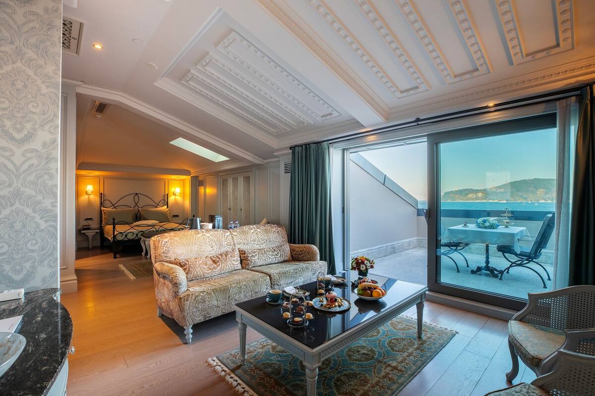 A spacious living room with a large sofa, a coffee table with snacks, and a view of the sea through a large window.