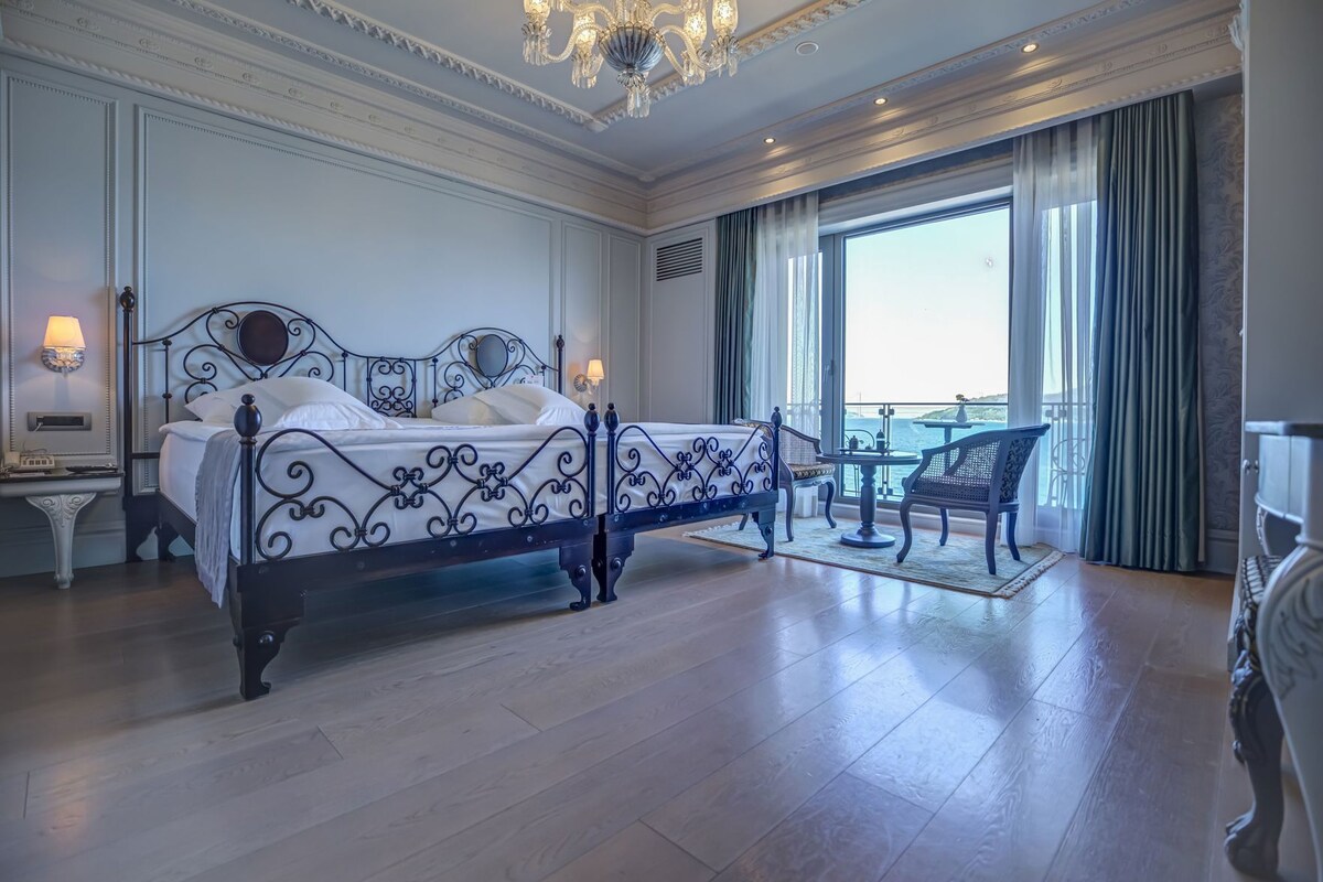 A spacious bedroom with a large bed, a balcony with a view, and a chandelier.