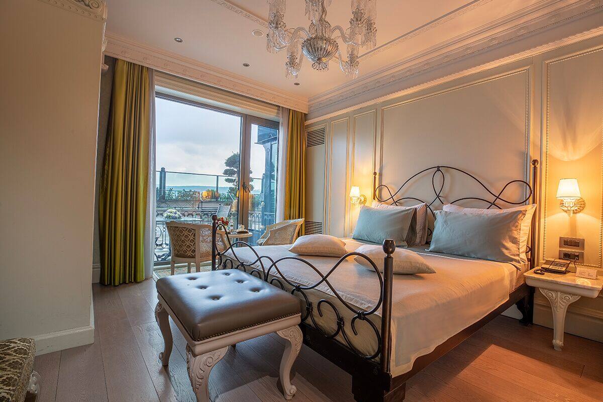 A hotel room with a large bed, a bench, a nightstand, and a view of the outside.