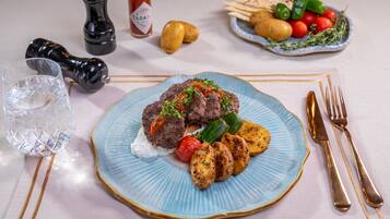 A plate of food with a blue rim, a glass of water, and a bottle of Tabasco sauce on a table.