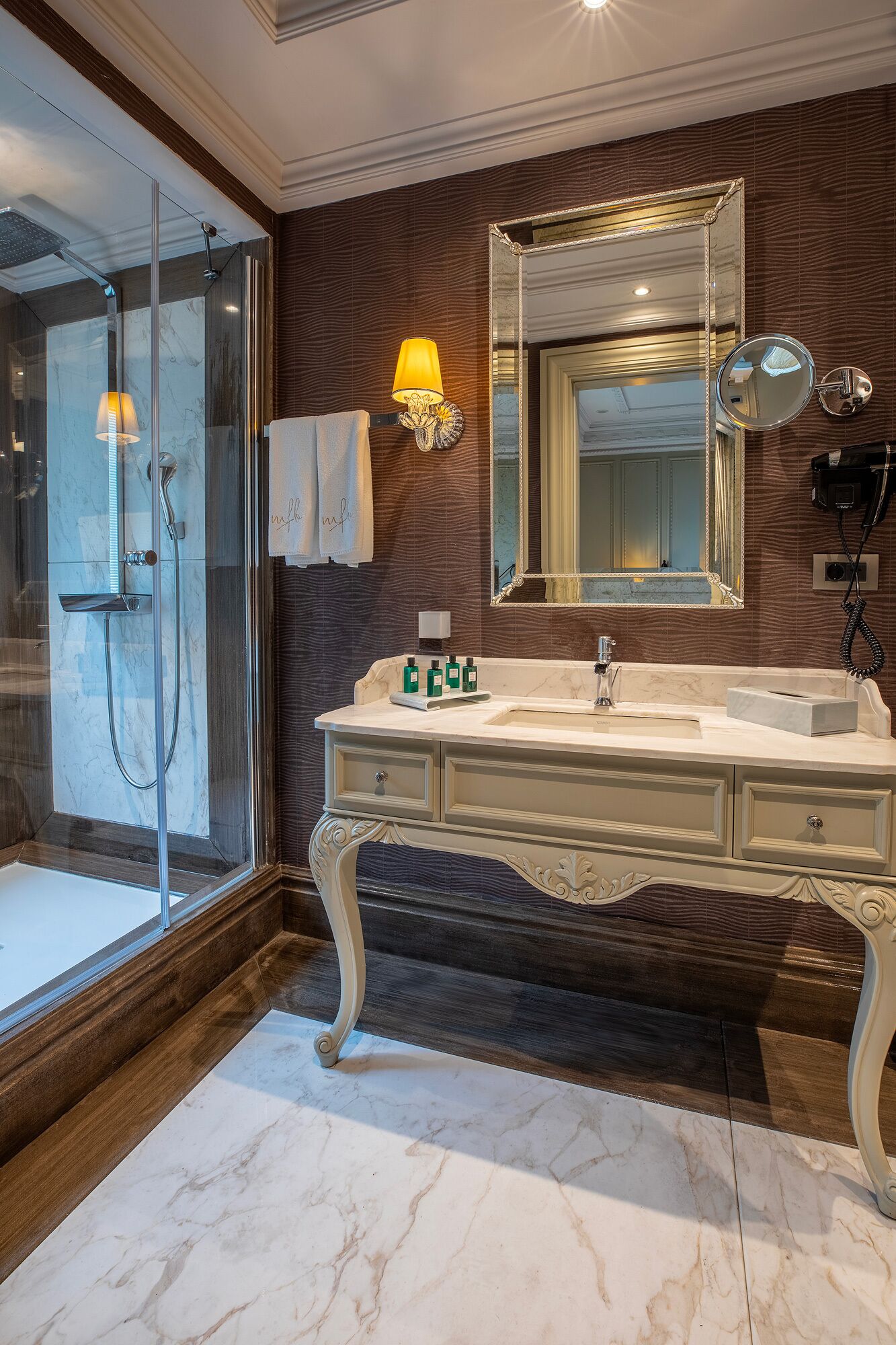 Une salle de bain avec un meuble-lavabo en marbre, un grand miroir, une douche avec des portes en verre et un porte-serviettes.