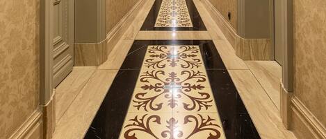 Un largo pasillo de hotel, estrecho, con paredes con diseño y suelo de baldosas negras y beige.