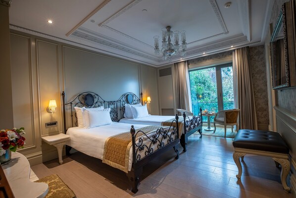 A hotel room with two beds, a chandelier, a balcony with a chair, and a view of greenery.