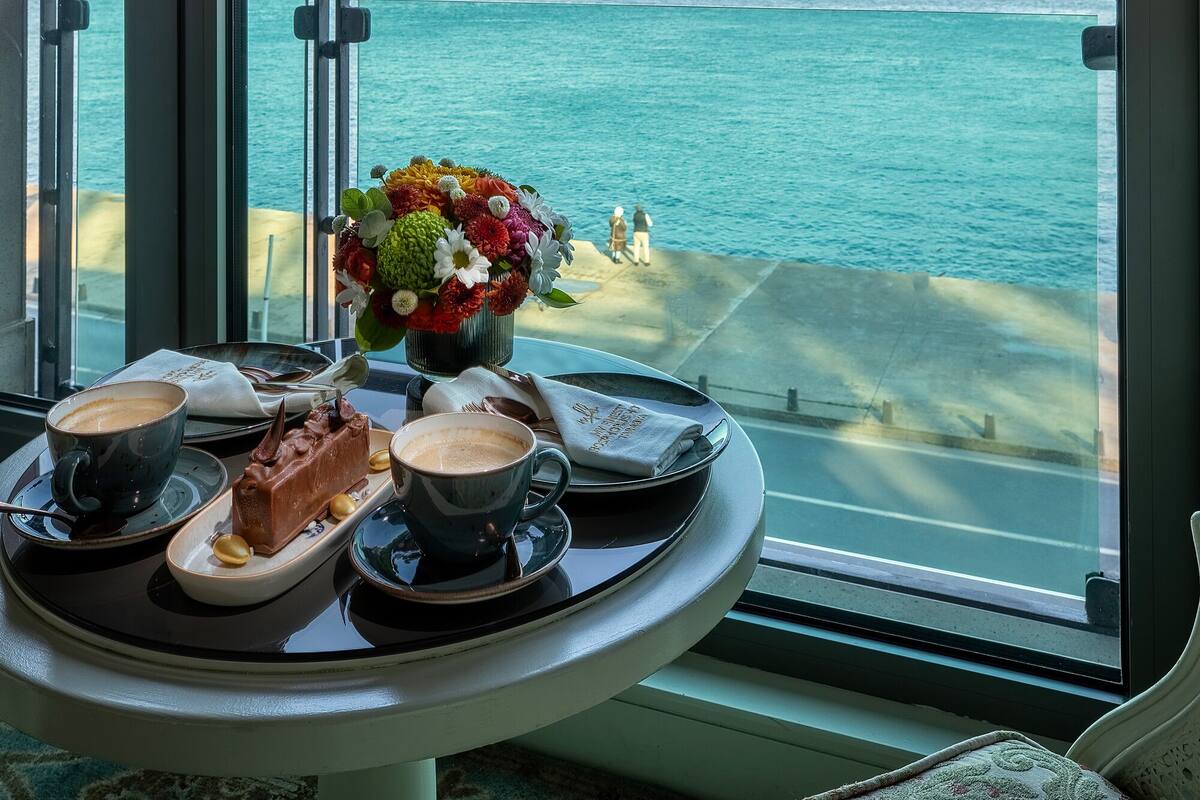 A table with a dessert, coffee, and a flower arrangement, overlooking a coastal view.