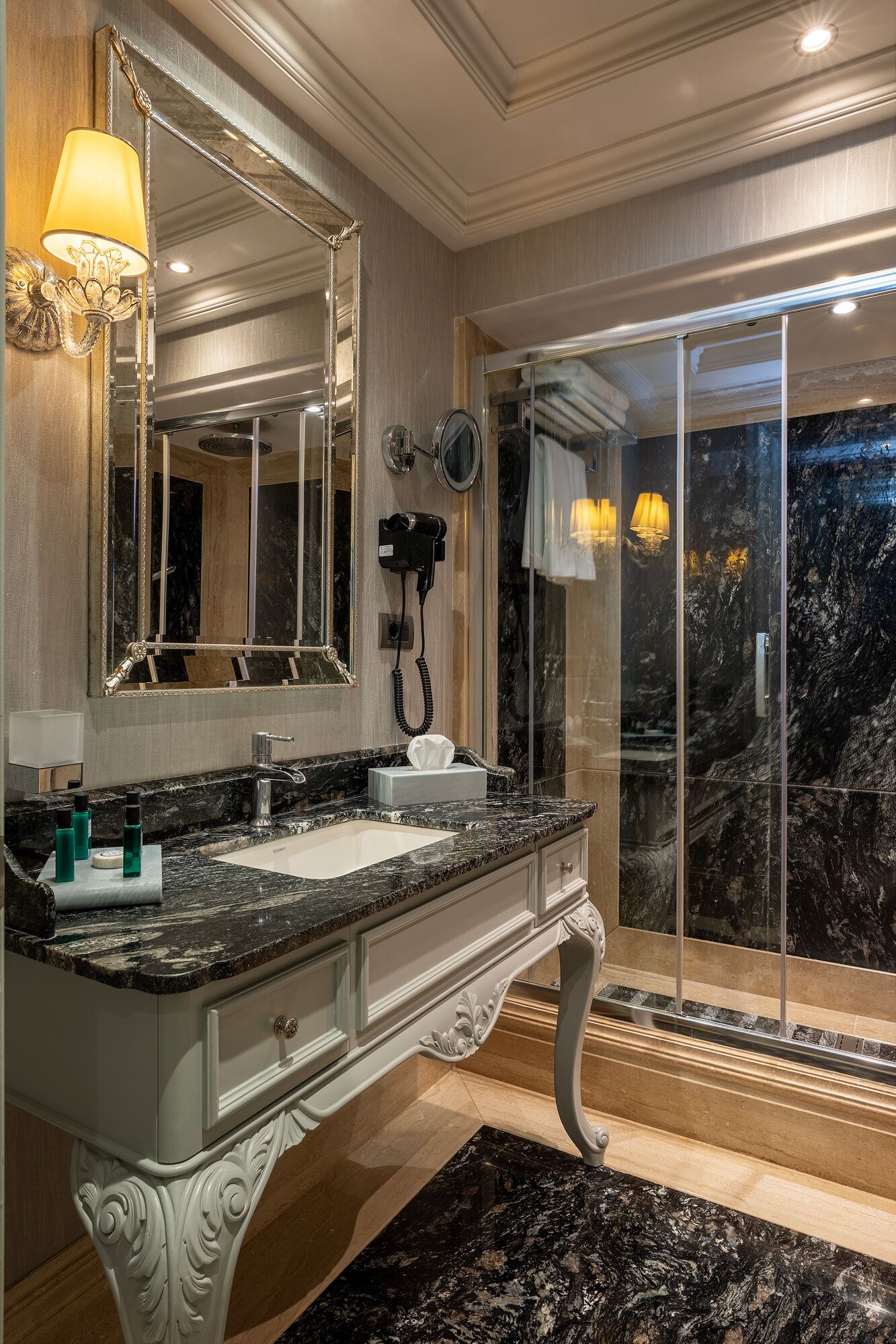 A luxurious bathroom with a marble sink, a large mirror, and a glass shower enclosure.