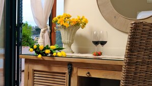 Una silla de mimbre con cojín, un aparador de madera con espejo, un jarrón con flores amarillas y dos copas de vino sobre una mesa.