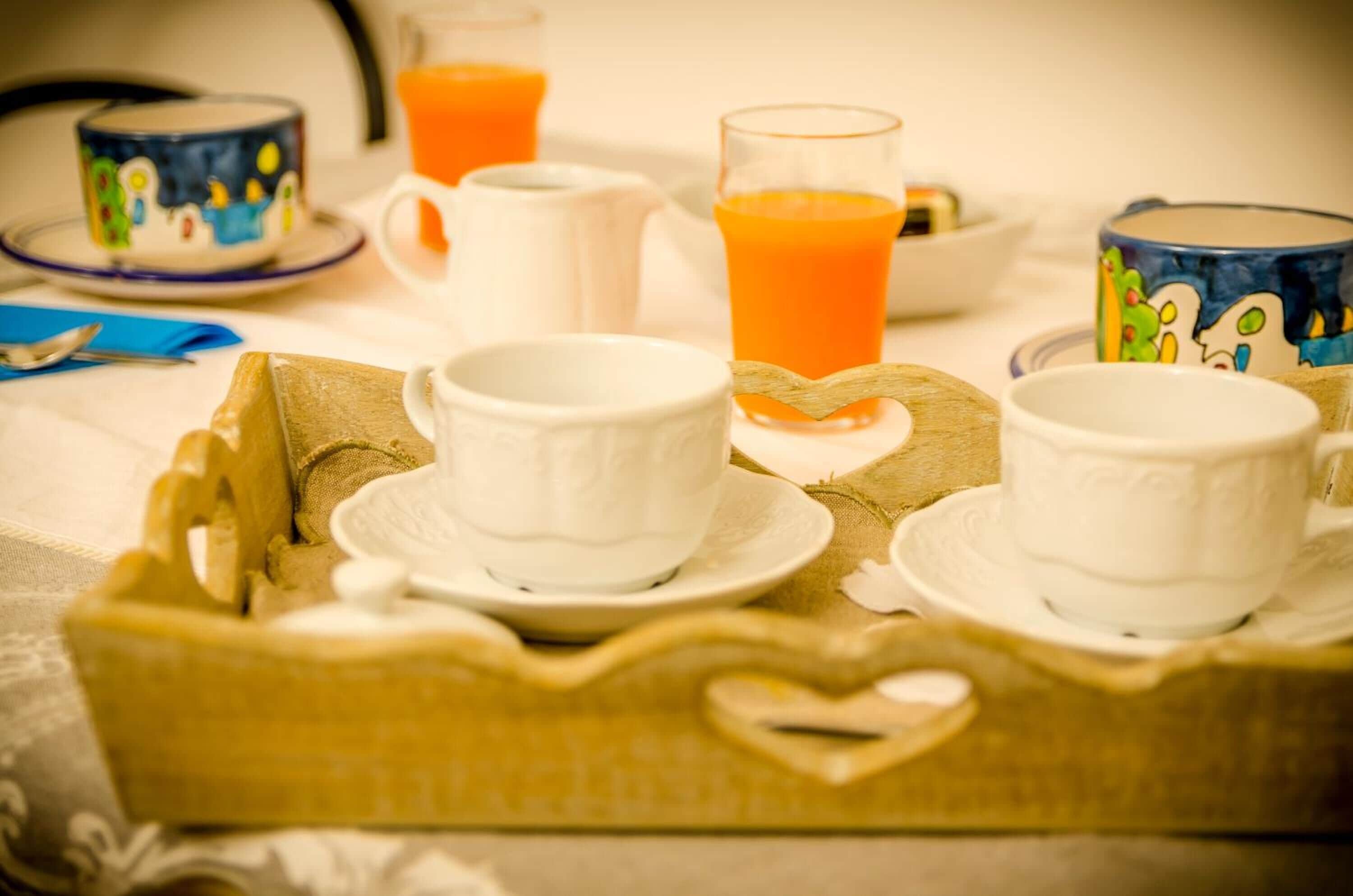 Bandeja de desayuno con tazas y un vaso de jugo de naranja sobre una mesa.