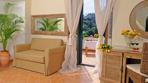 Una habitación acogedora con un sofá color beige, una planta en maceta, un espejo, una mesa con flores y vistas a un balcón con mesa y sillas.