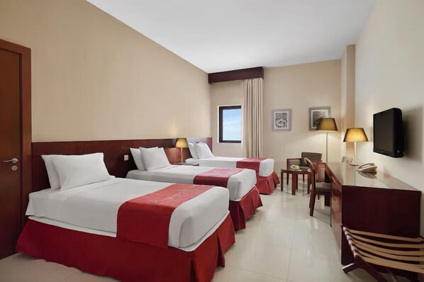 A hotel room with two beds, a desk, a chair, a television, and a window.