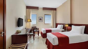 Habitación de hotel con dos camas, un escritorio, una silla, un televisor y dos ventanas con cortinas.
