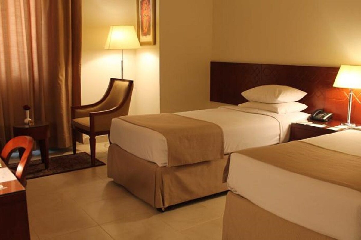 Une chambre d’hôtel avec deux lits, un bureau, une chaise et deux lampes de chevet.