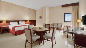 Ein Hotelzimmer mit einem Bett, einem runden Esstisch, Stühlen, einem Fernseher und einem Fenster.
