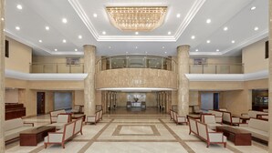 Eine geräumige Lobby mit einer zentralen Sitzgruppe, einem prächtigen Kronleuchter und einem Glasgeländer, das auf die untere Ebene blickt.