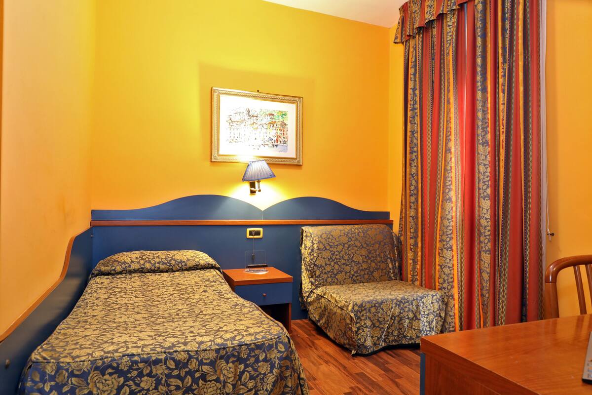 Une chambre d’hôtel avec deux lits, une table de chevet en bois, une lampe, une chaise et une table.