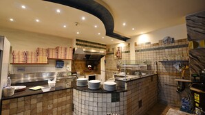 A kitchen with a tiled backsplash, a pizza oven, and stacks of pizza boxes. - Albergo Al Castello (Pomezia)