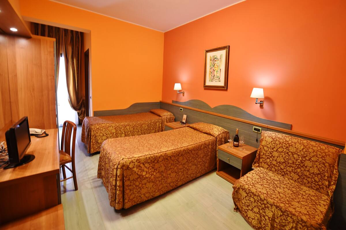 Une chambre d’hôtel avec deux lits simples, un bureau avec un ordinateur et une chaise.