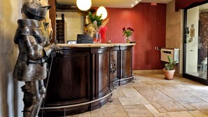 A reception area with a dark wooden reception desk, a knight statue, and a potted plant. - Albergo Al Castello (Pomezia)
