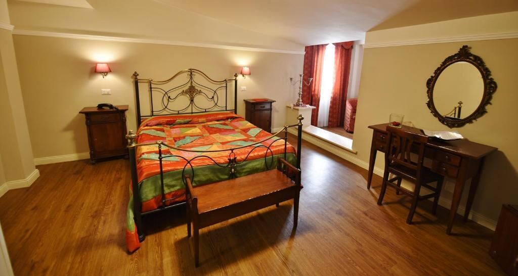 A bedroom with a bed, bedside tables, a dresser, a mirror, and a window with curtains.