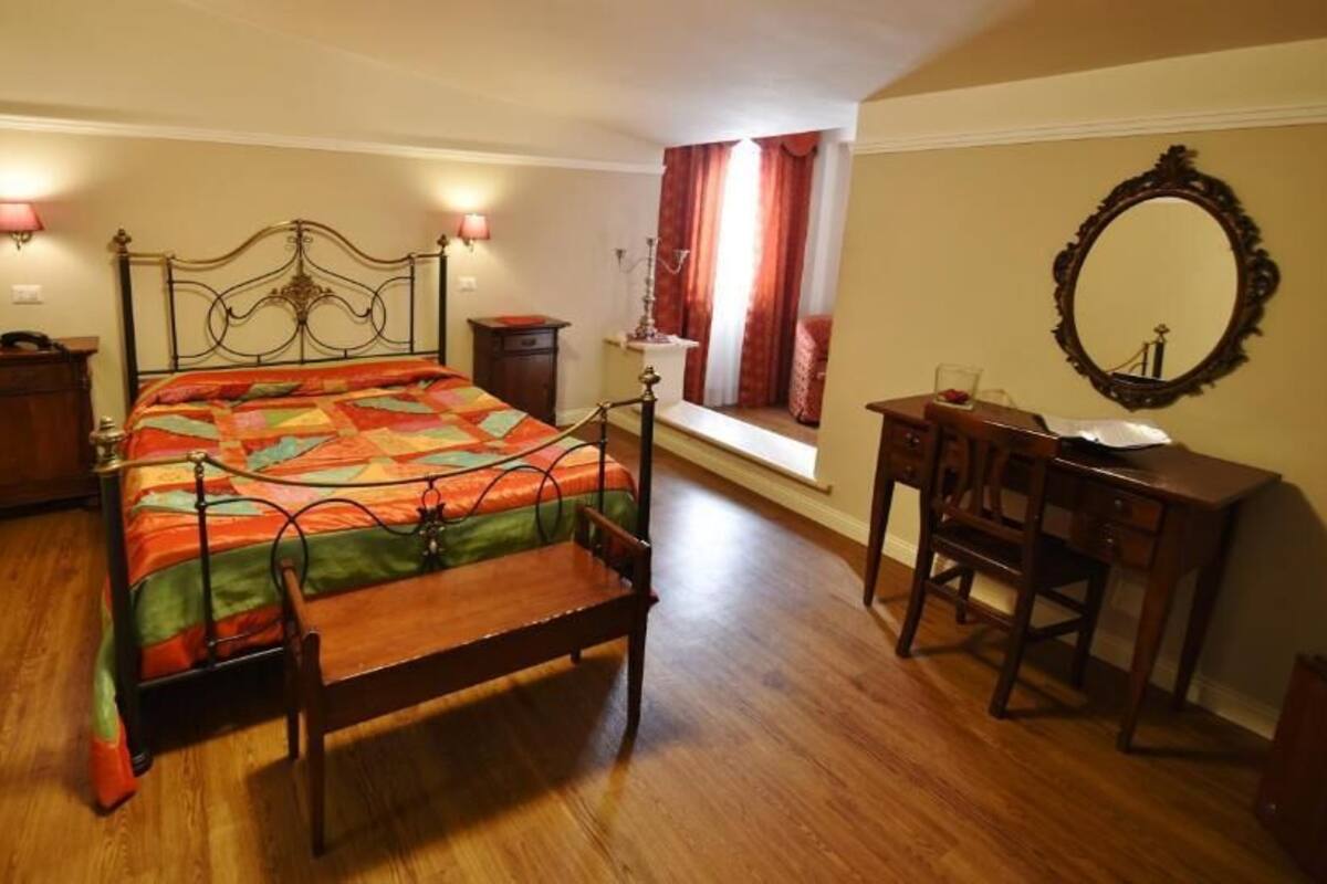 Une chambre à coucher avec un lit, des tables de chevet, une commode, un miroir et une fenêtre avec des rideaux.