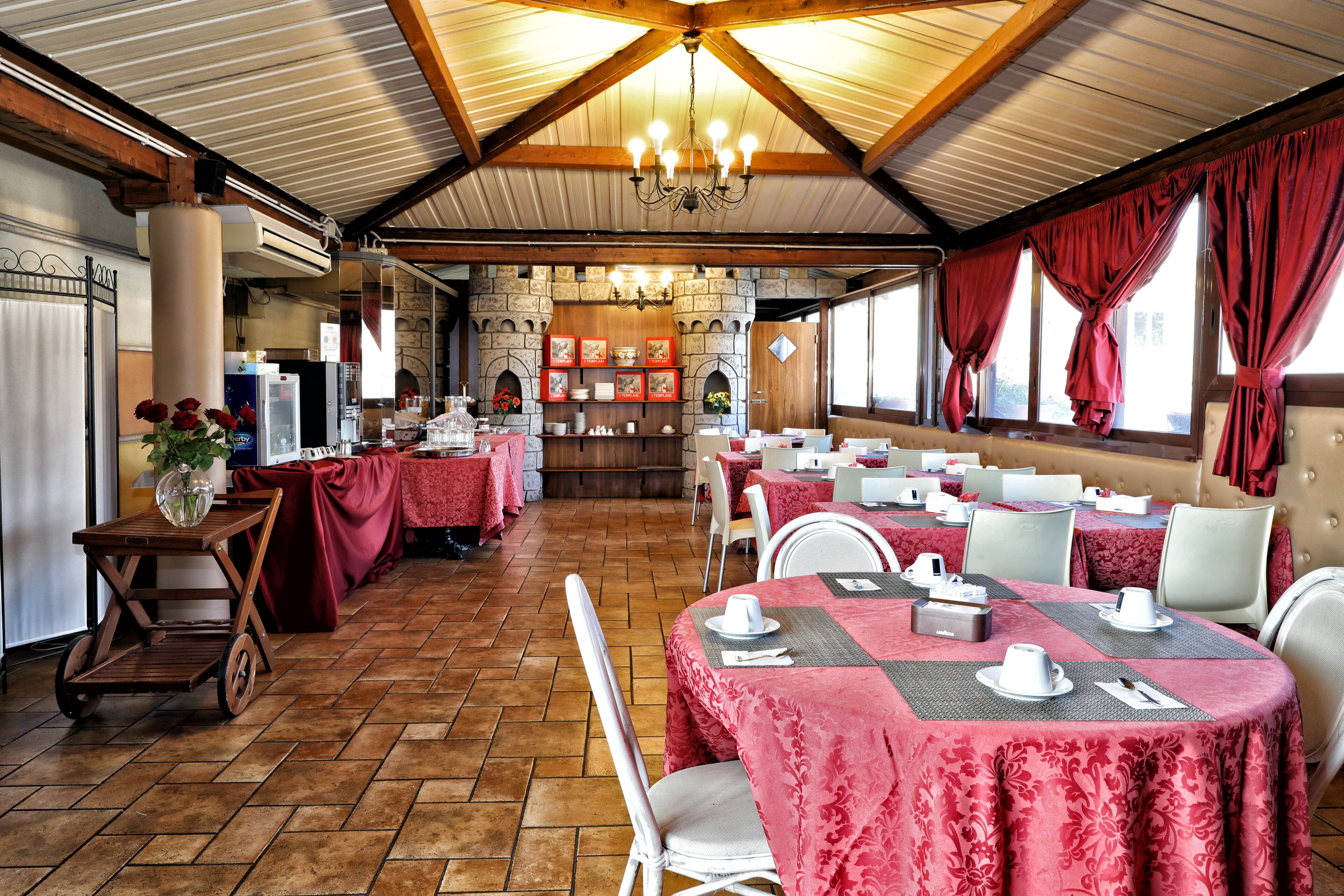 A restaurant with round tables covered in red tablecloths, white chairs, and a wooden ceiling with exposed beams.